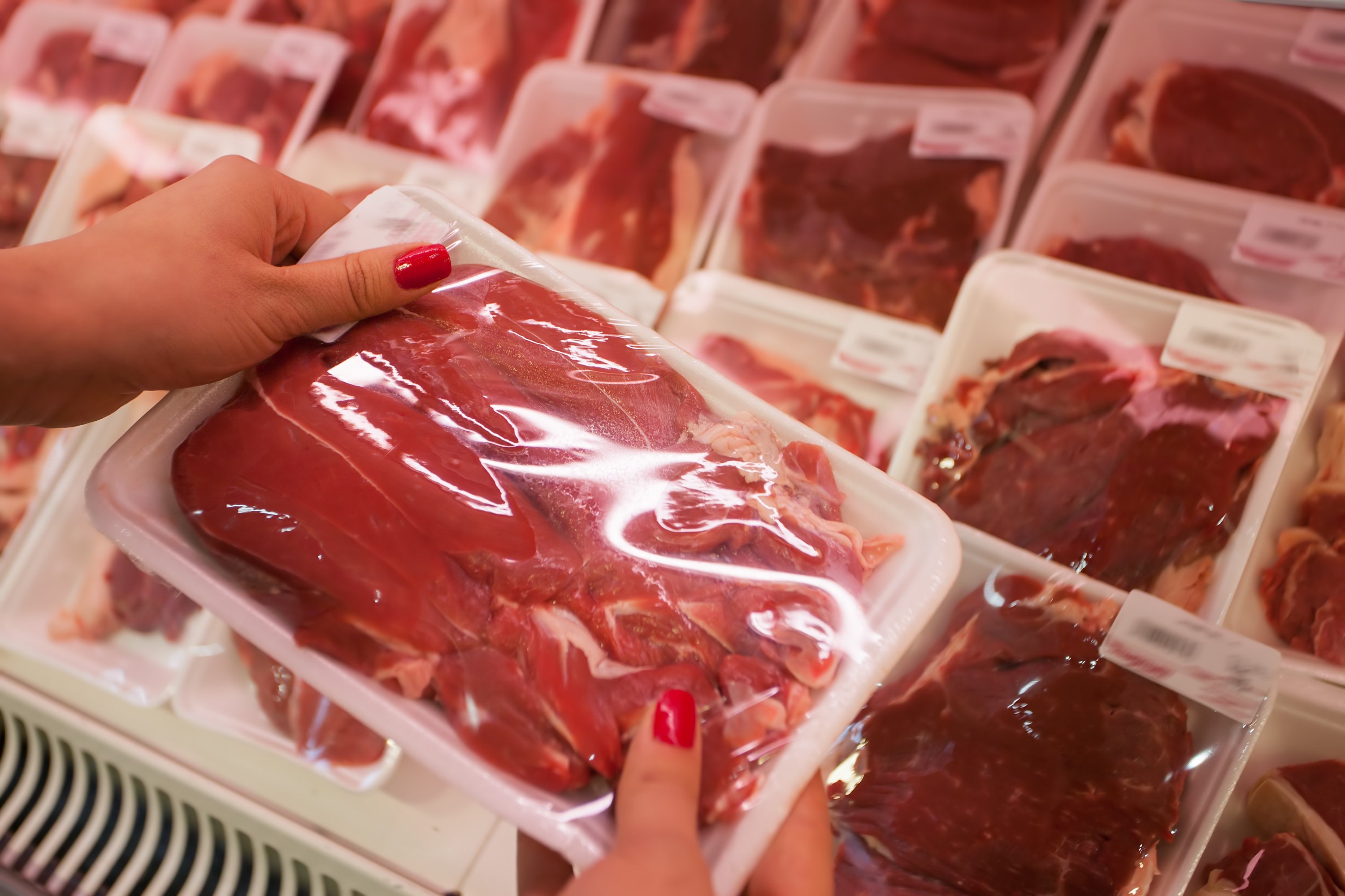A woman's hands holding a package of pork, with more pork products in the background.