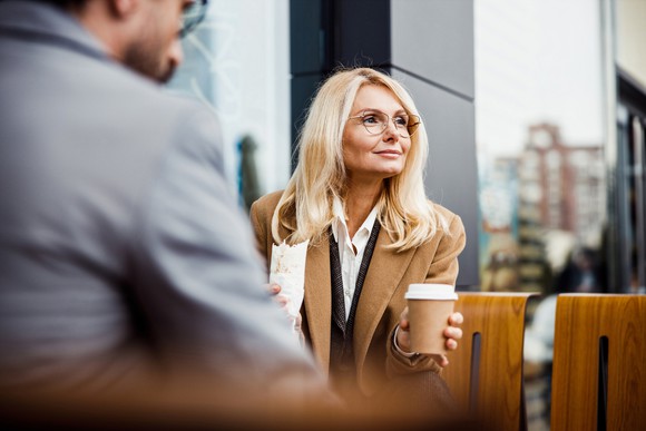 A businesswoman holds a cup of coffee in one hand and a burrito in the other. 