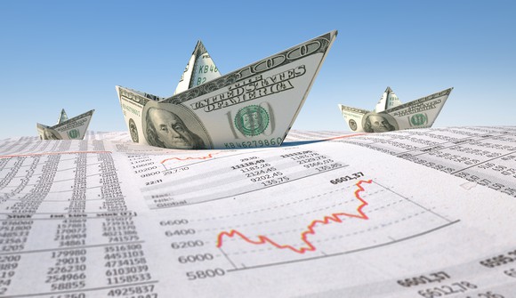 Three boats made from $100 bills on top of stock data and a stock chart.