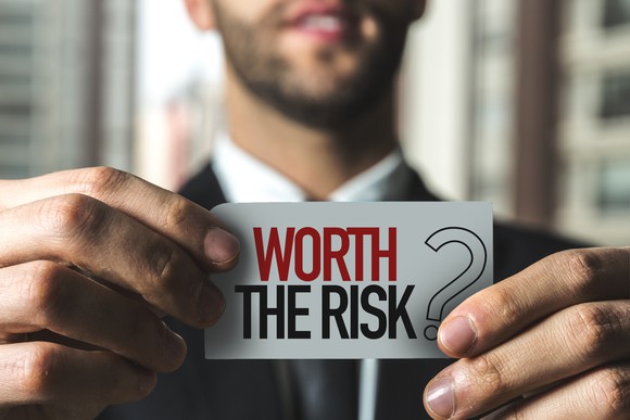 A young man in a suit holds up a sign that says worth the risk? 