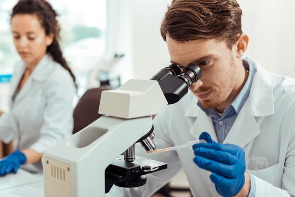 A scientist peers into a microscope while applying liquid with a pipette.