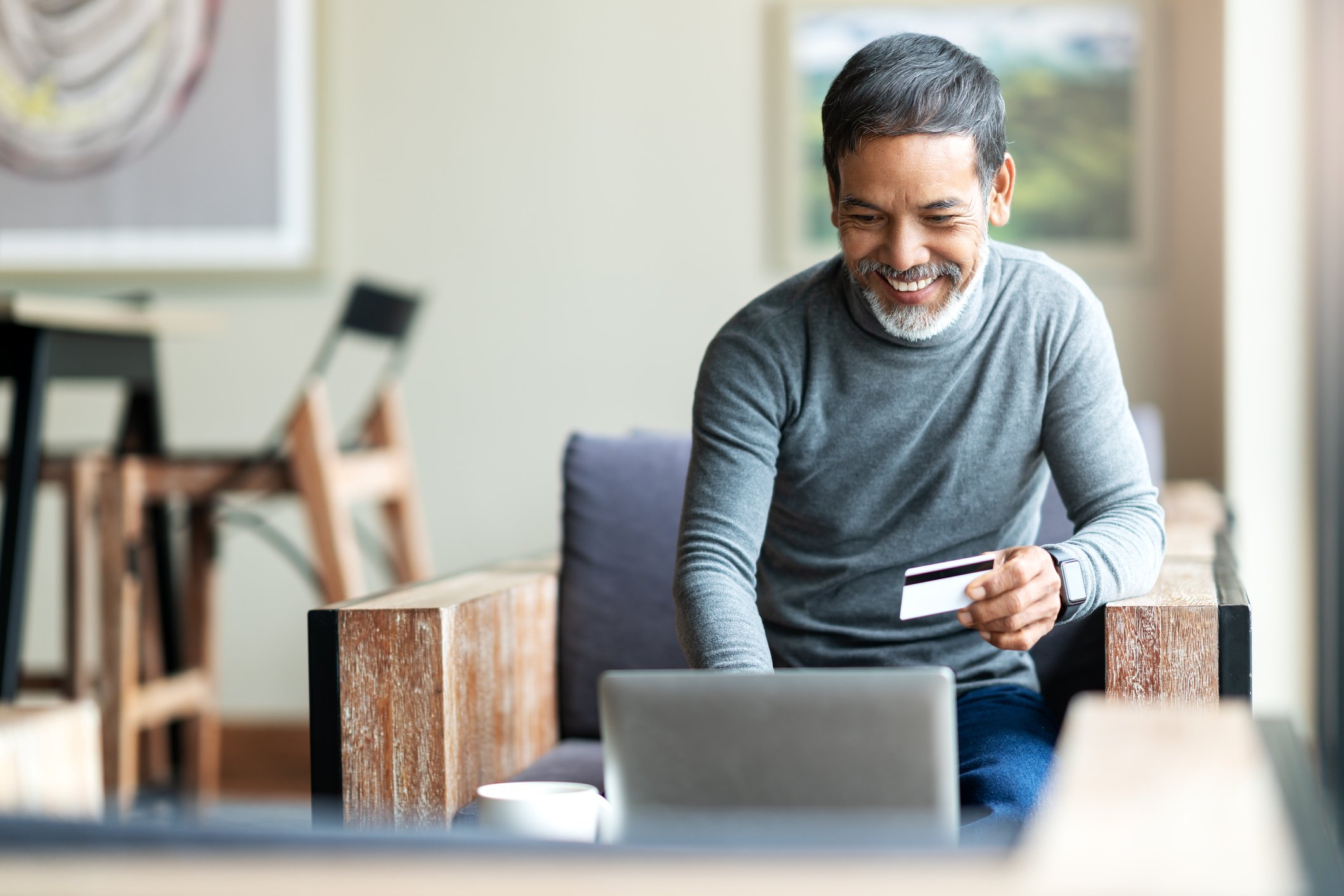 Man smiling while using his laptop and holding a credit card in his left hand. 