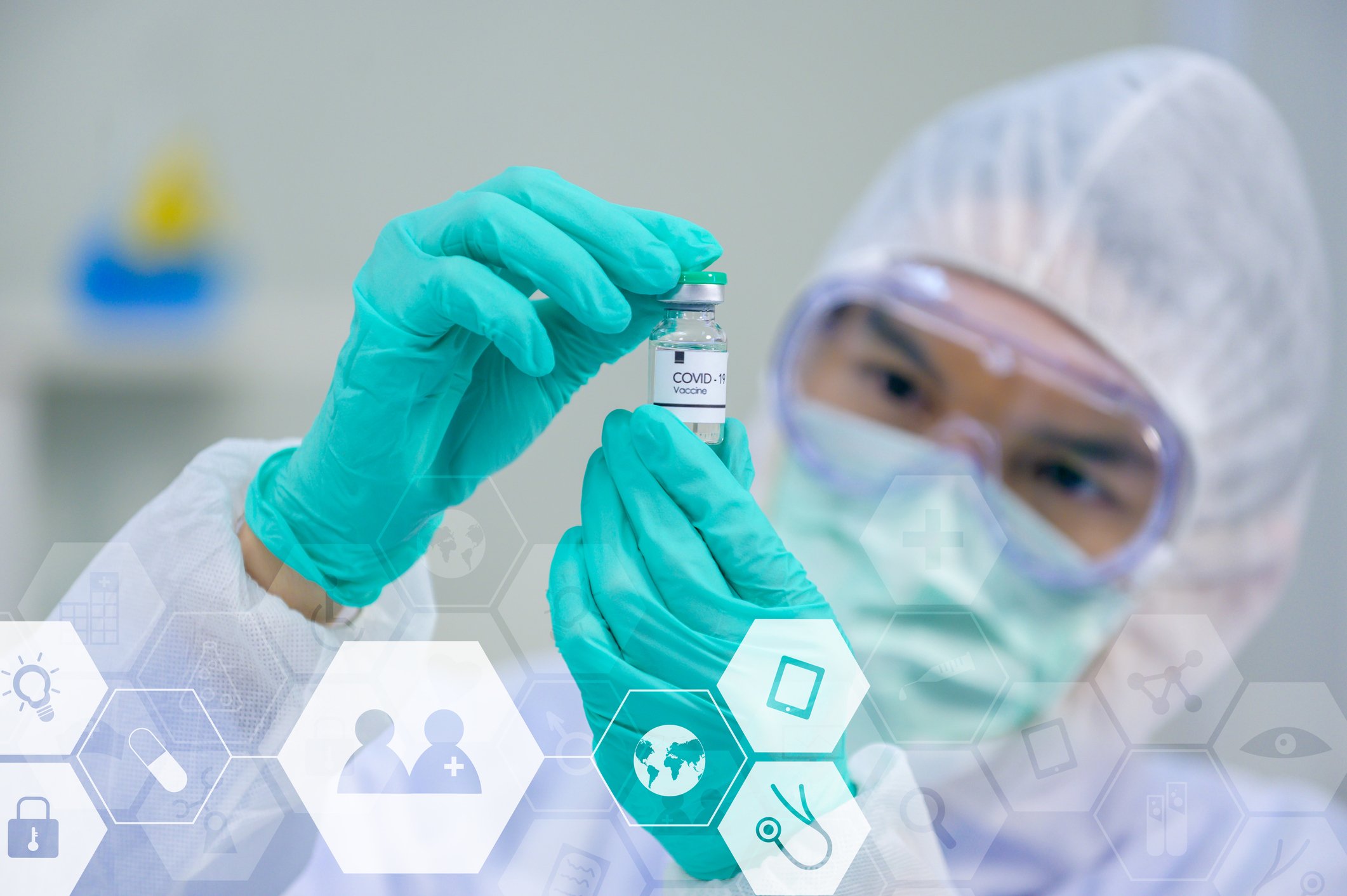Scientist in protective gear holding a vial labeled COVID-19 Vaccine