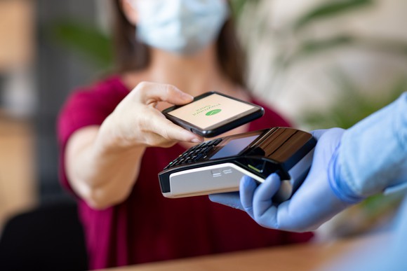 A woman wearing a mask making a contactless payment with her phone.