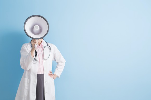 A woman in a lab coat speaks through a megaphone.