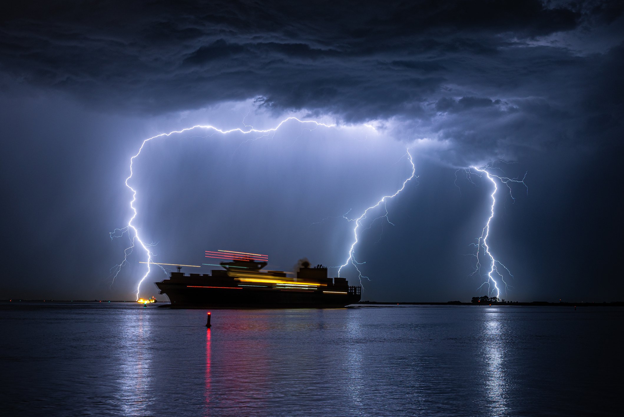 A large modern ship during a storm, with three strokes of lightning in the background.