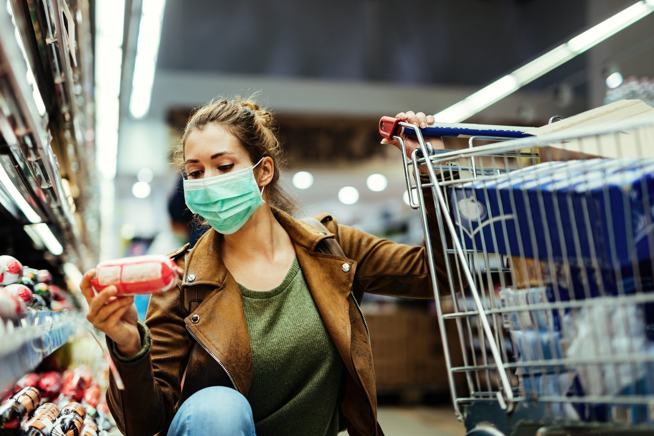 A shopper in a mask inspects a product in a grocery store. 
