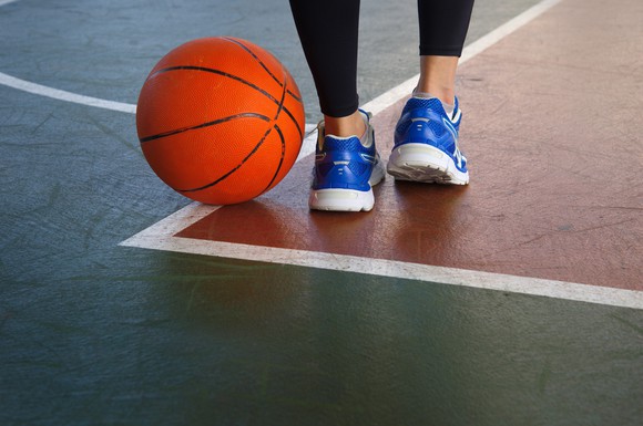 A woman in blue sports shoes standing next to a basketball on the court.