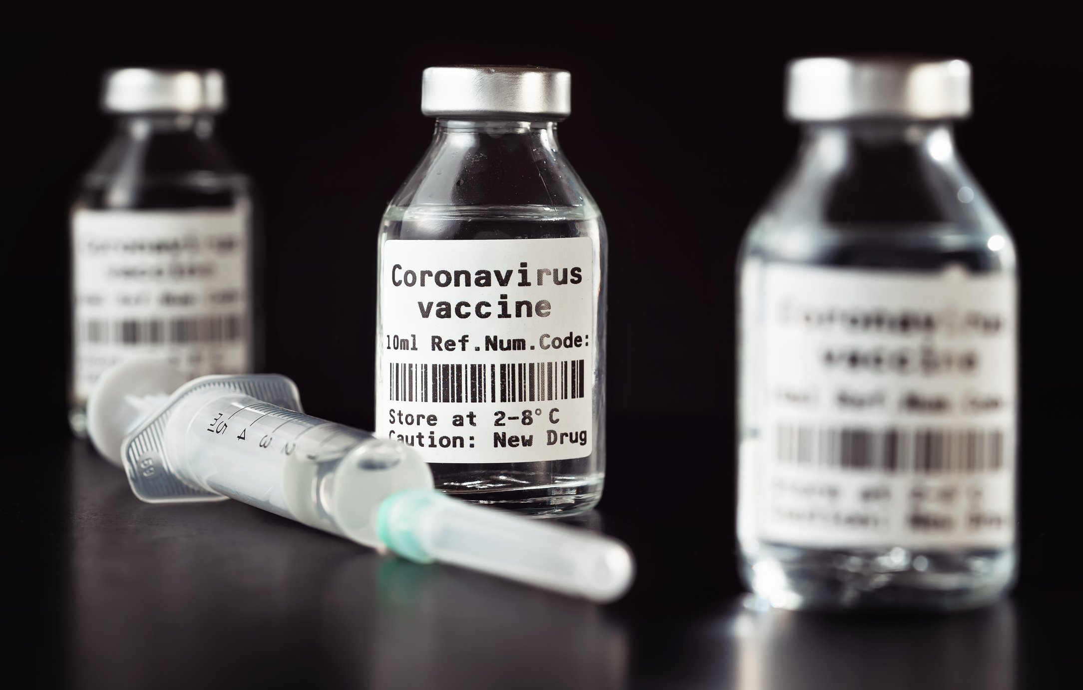 Three vaccine bottles that say Coronavirus vaccine next to a syringe.
