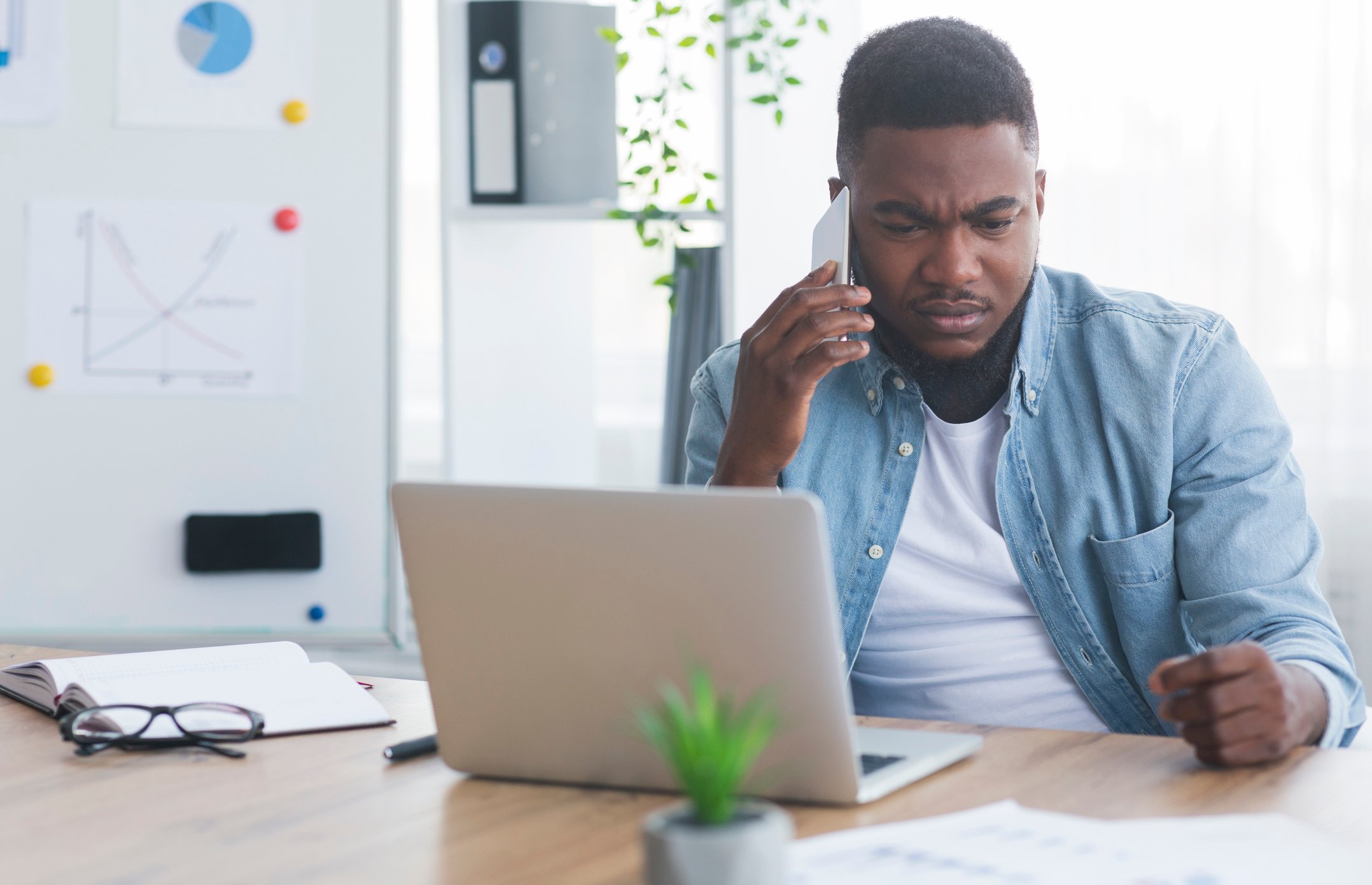 A person on their cellphone sitting in front of a laptop. 