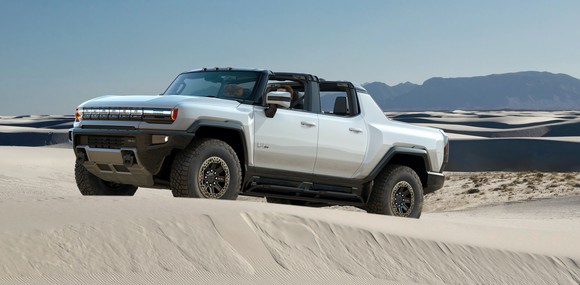 A silver GMC Hummer EV, a big electric off-road truck, shown on a sand dune.