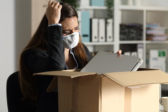 A woman wearing a mask and an anguished look on her face is packing a box.