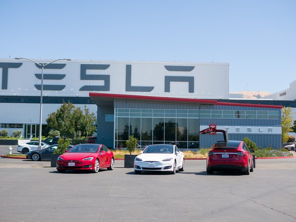 Three Tesla cars in parking lot in front of Tesla factory.