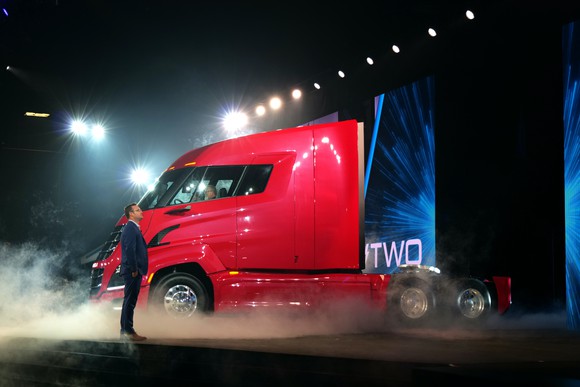 Milton is shown standing on an auto-show stage with a red Nikola Two, an electric semi truck.