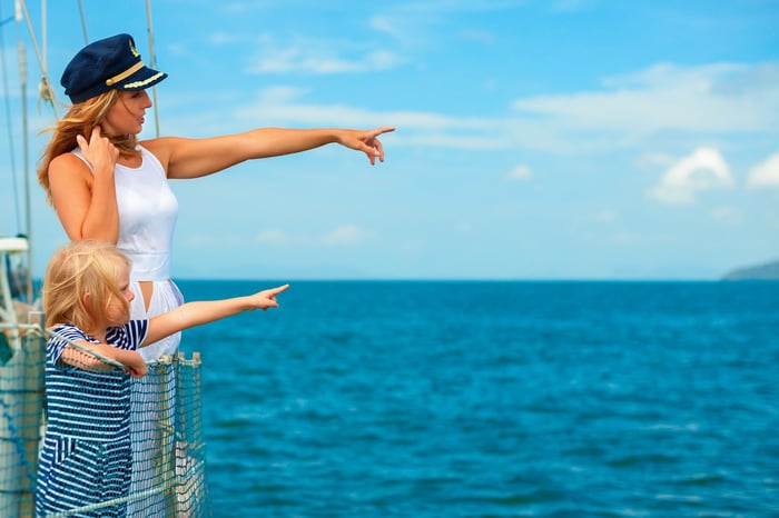 Two people on a ship, pointing to an island in the distance.