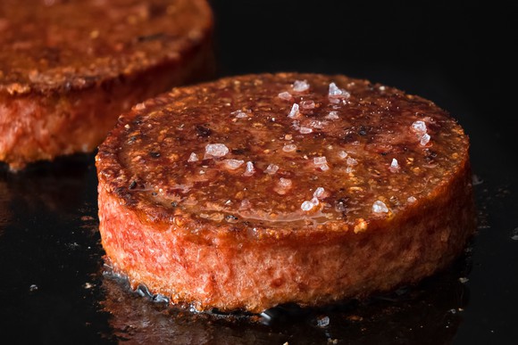 A plant-based burger sizzles on an hot oven top. 