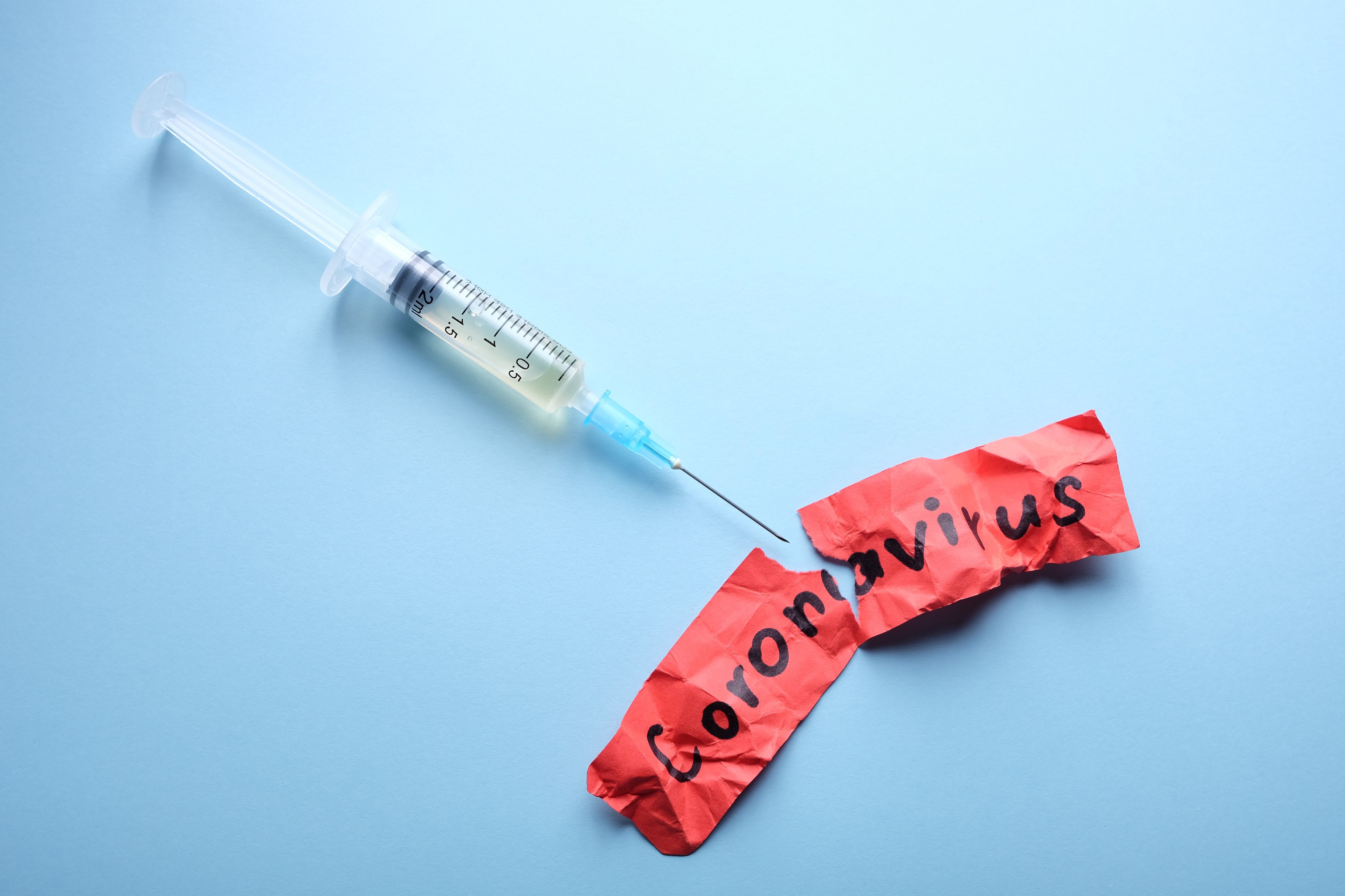 Syringe and torn piece of paper with Coronavirus written on it. 