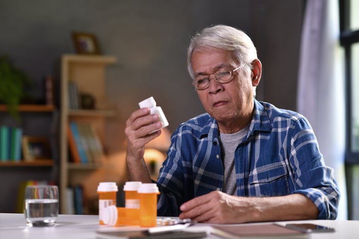 Elderly person at a table with bottles of pills.