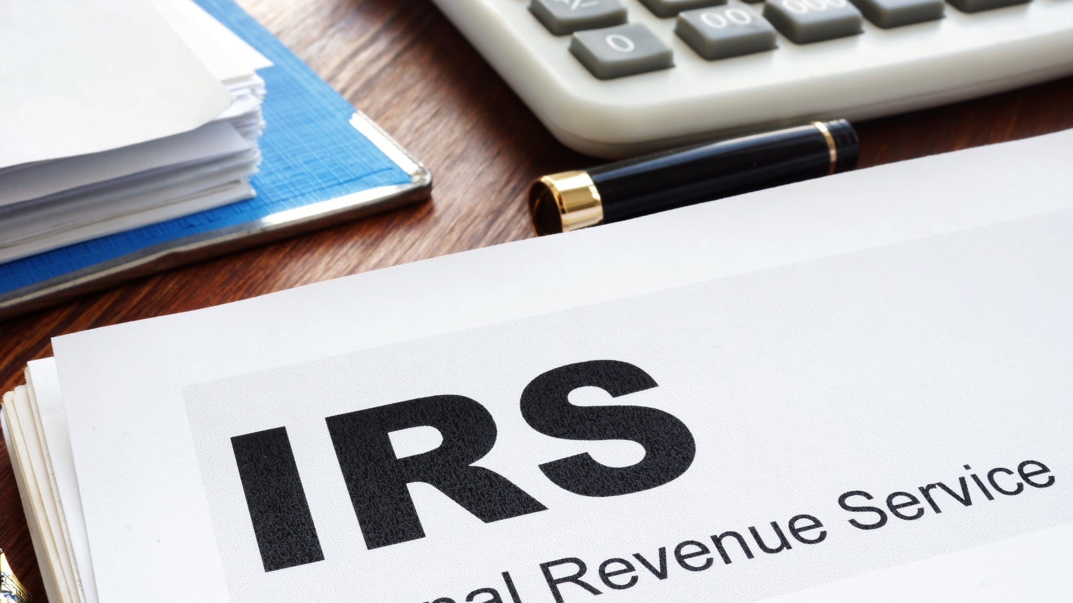 Paper labeled IRS and Internal Revenue Service, on desk with calculator and pen.
