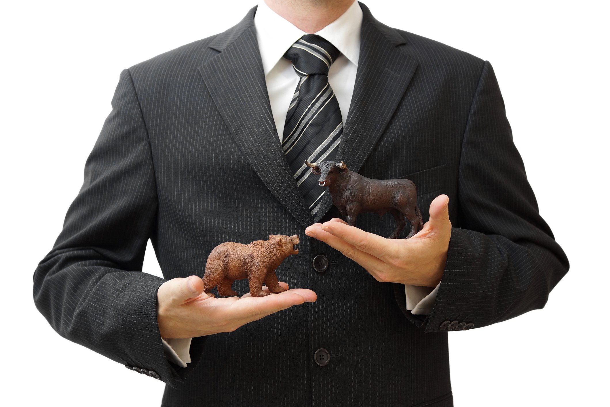 Businessman holding a tiny bear and a tiny bull figurine.