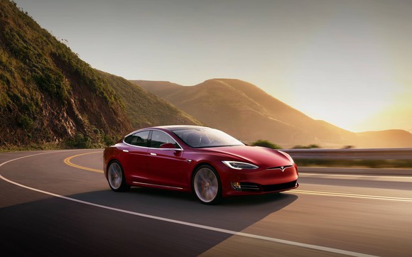 Red Model S driving along a curved road with mountains and sun in the background