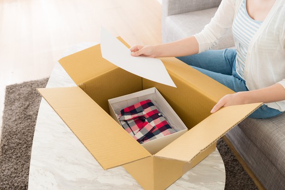 A woman opening a box with a shirt in it and looking at a piece of paper