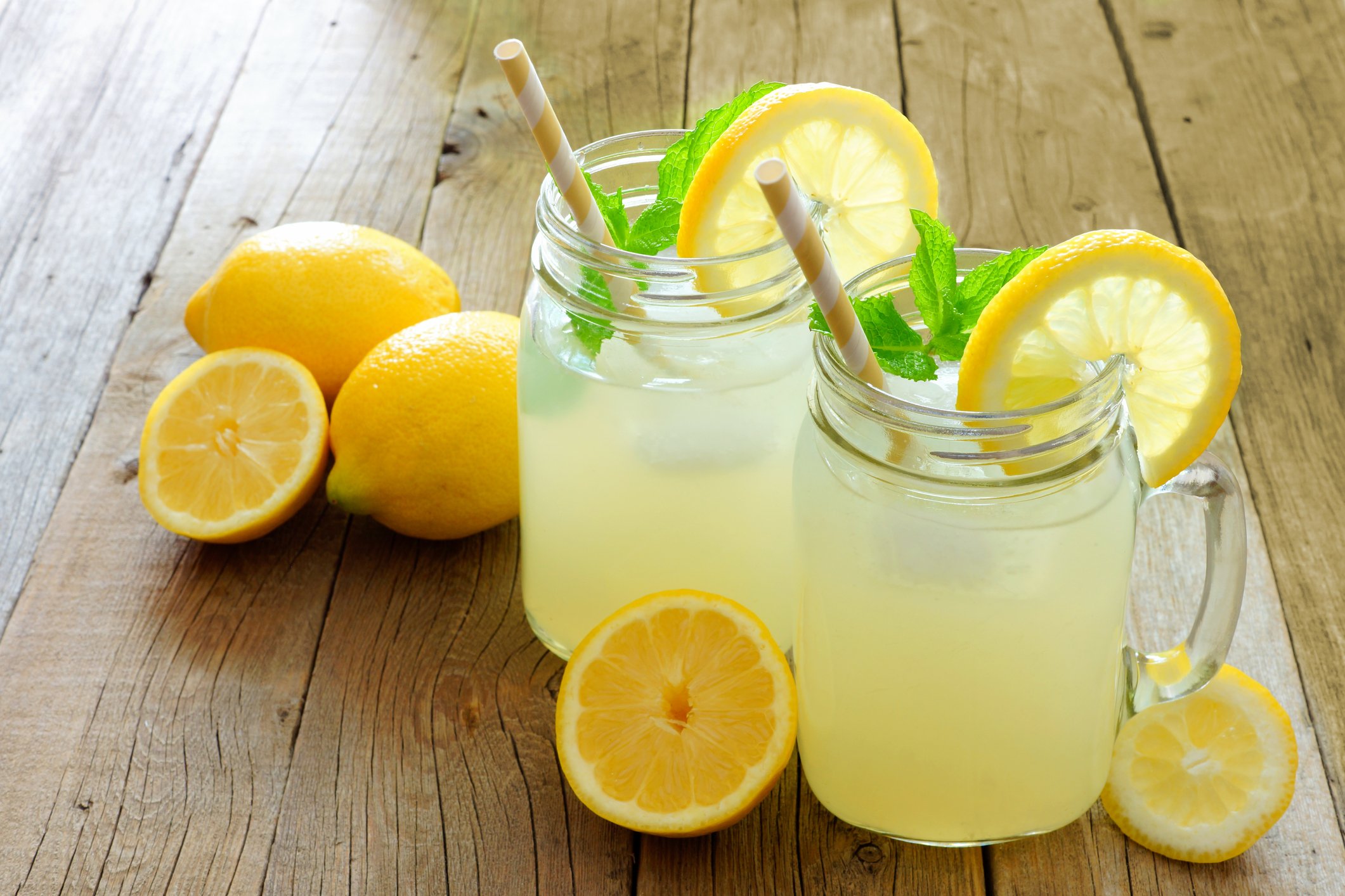 Two jars of lemonade on a table with whole lemons and lemon slices. 