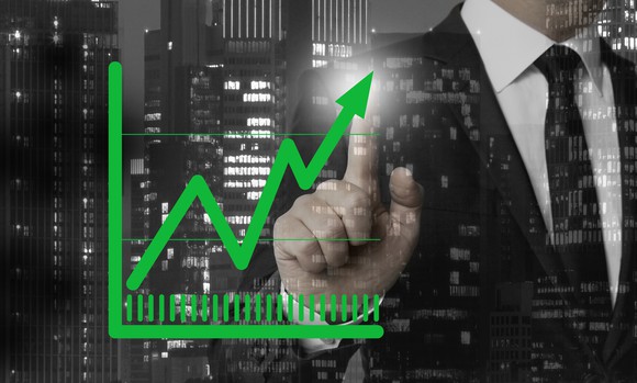 Man in suit pointing at screen showing upward green arrow on chart 