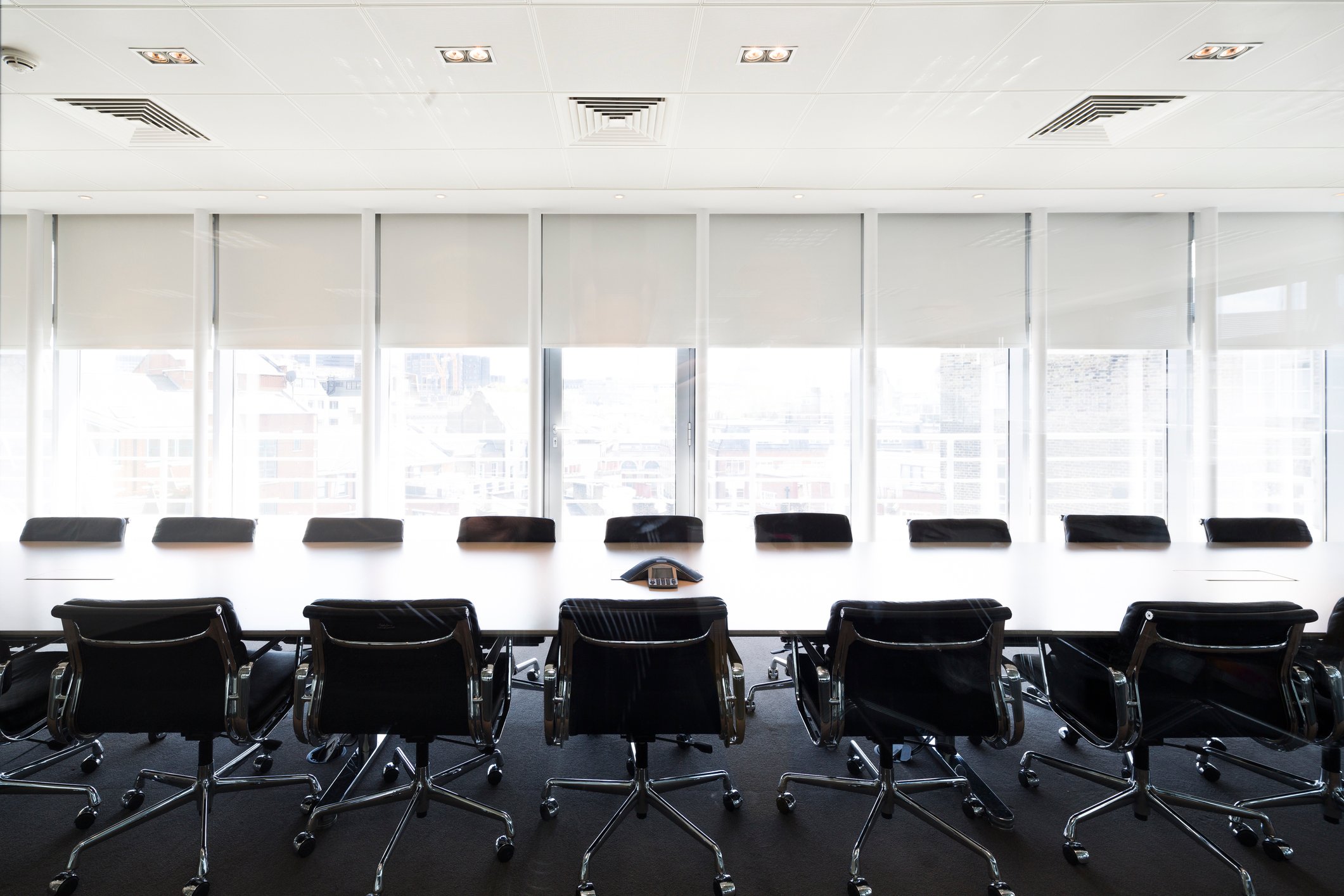 An ultramodern corporate boardroom with rows of chairs flanking a long polished tabletop.