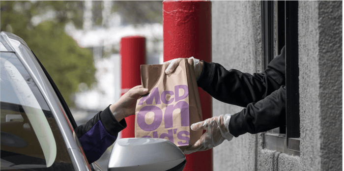 Customer reaching out of car to receive McDonald's order from employee offering it out of the drive-thru window