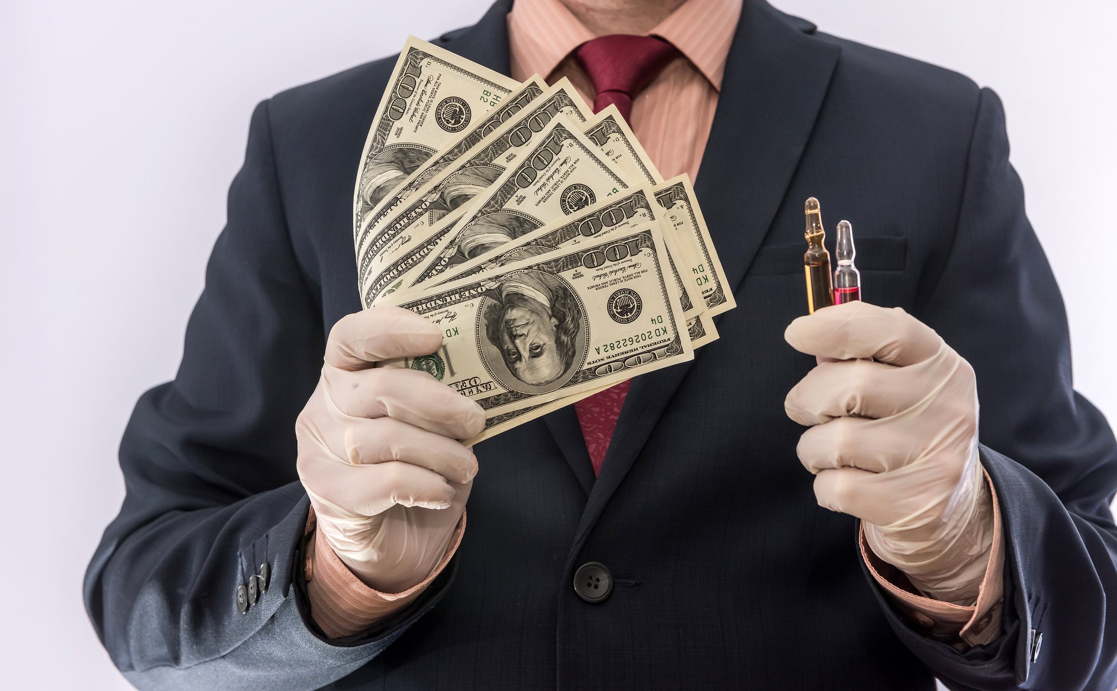 Man in suit wearing gloves holding cash and vials 