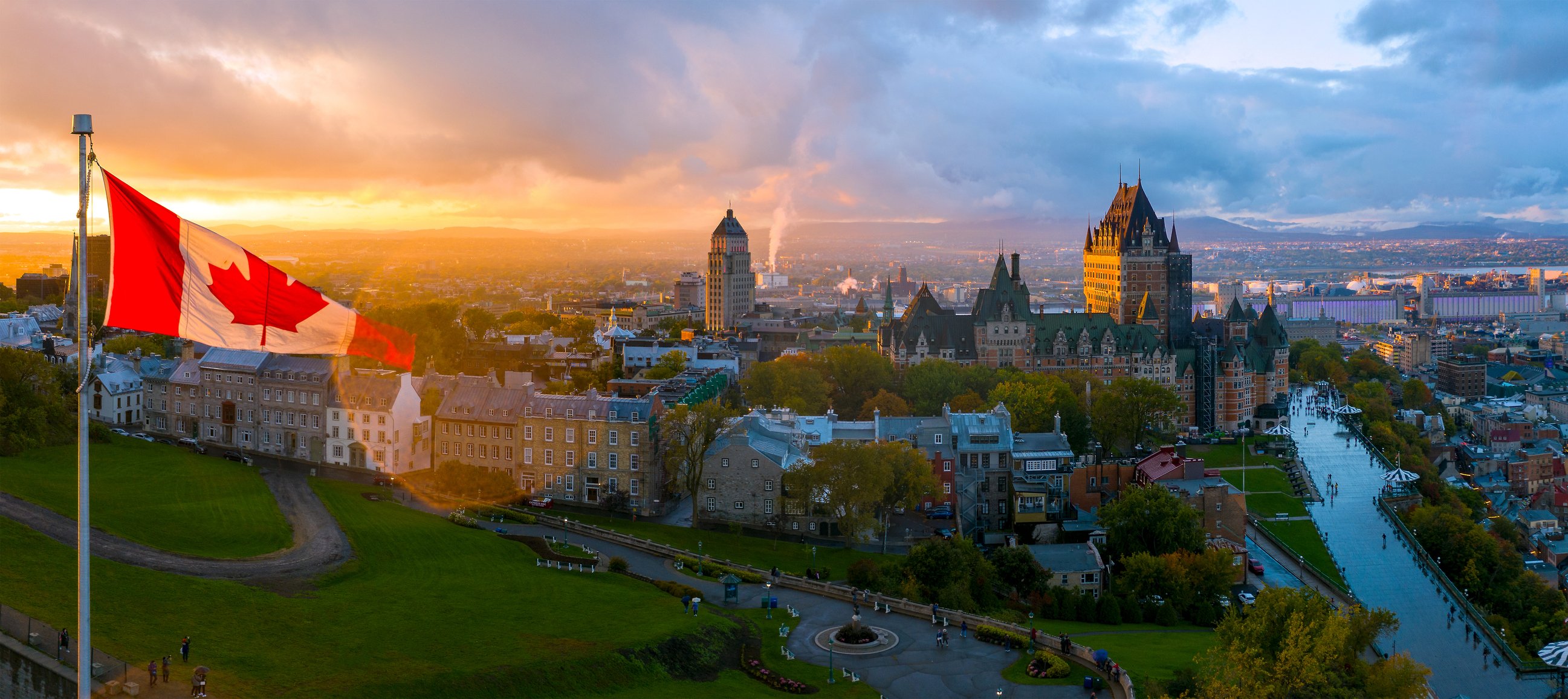 The Canadian flag flying over Quebec with a sunset sky in the background.
