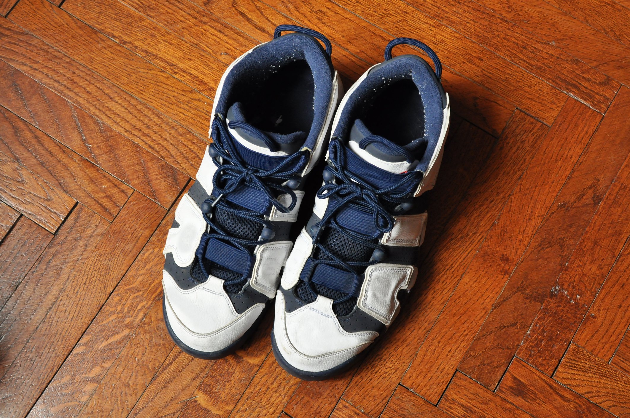 A pair of blue and white basketball shoes on a herringbone wood floor.