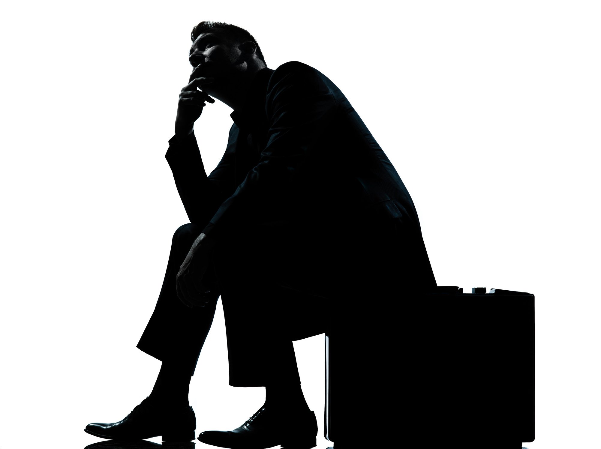 Silhouette of a businessperson in deep thought, seated on their briefcase.