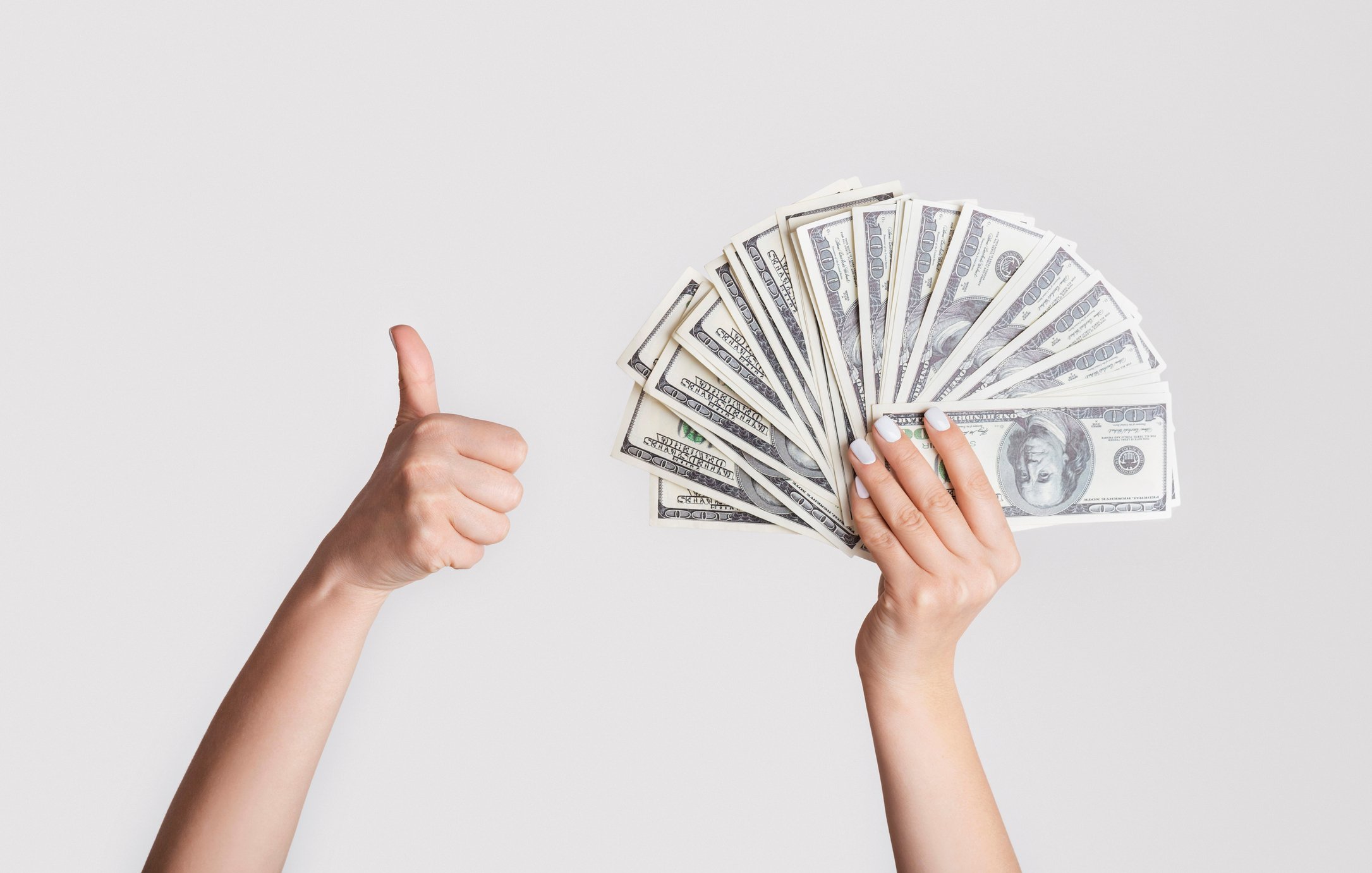 One hand with a thumb up and the other hand holding cash fanned out