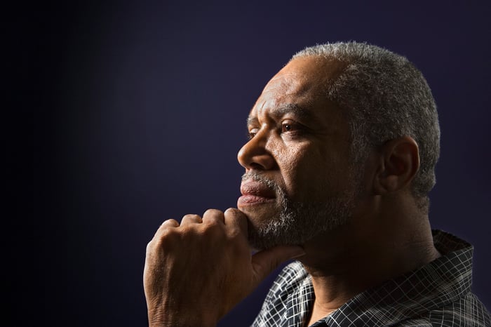 A senior man thinks as he rests his chin on his hand.