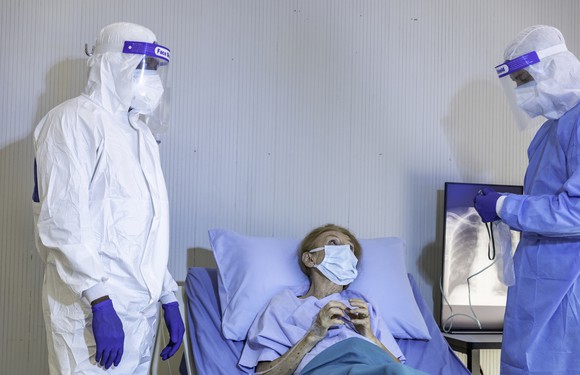 Doctors in protective gear talking to a patient in a mask