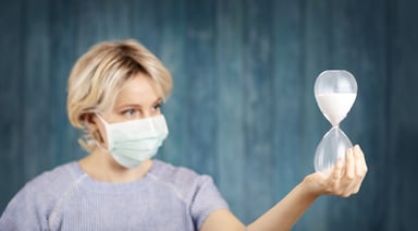 Woman wearing mask looking at hourglass