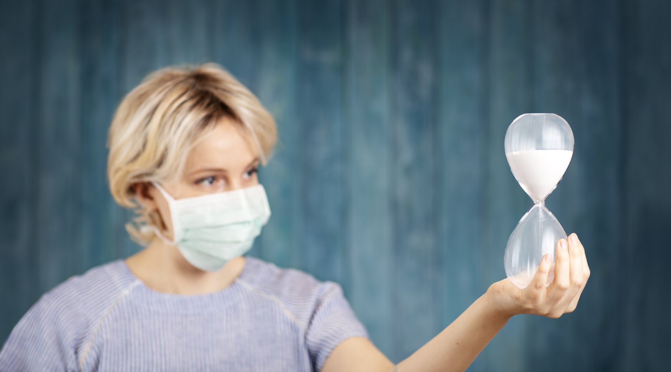 Woman wearing a mask holding a large hourglass. 