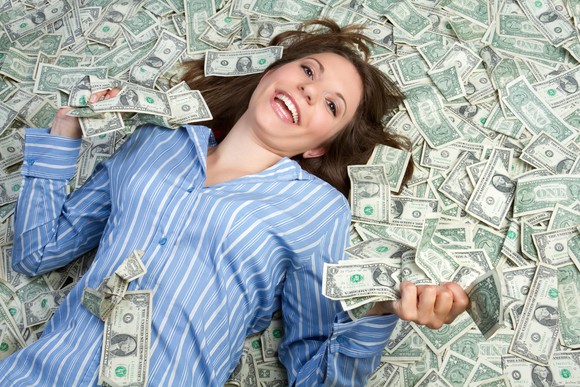 Smiling woman lying on a pile of U.S. cash. 