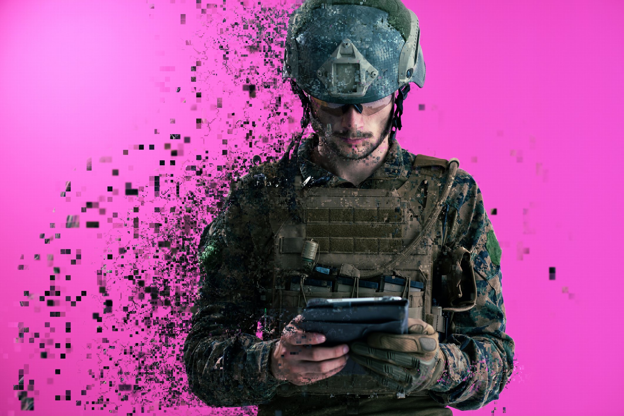 A soldier in fatigues holds a tablet against a magenta background. 