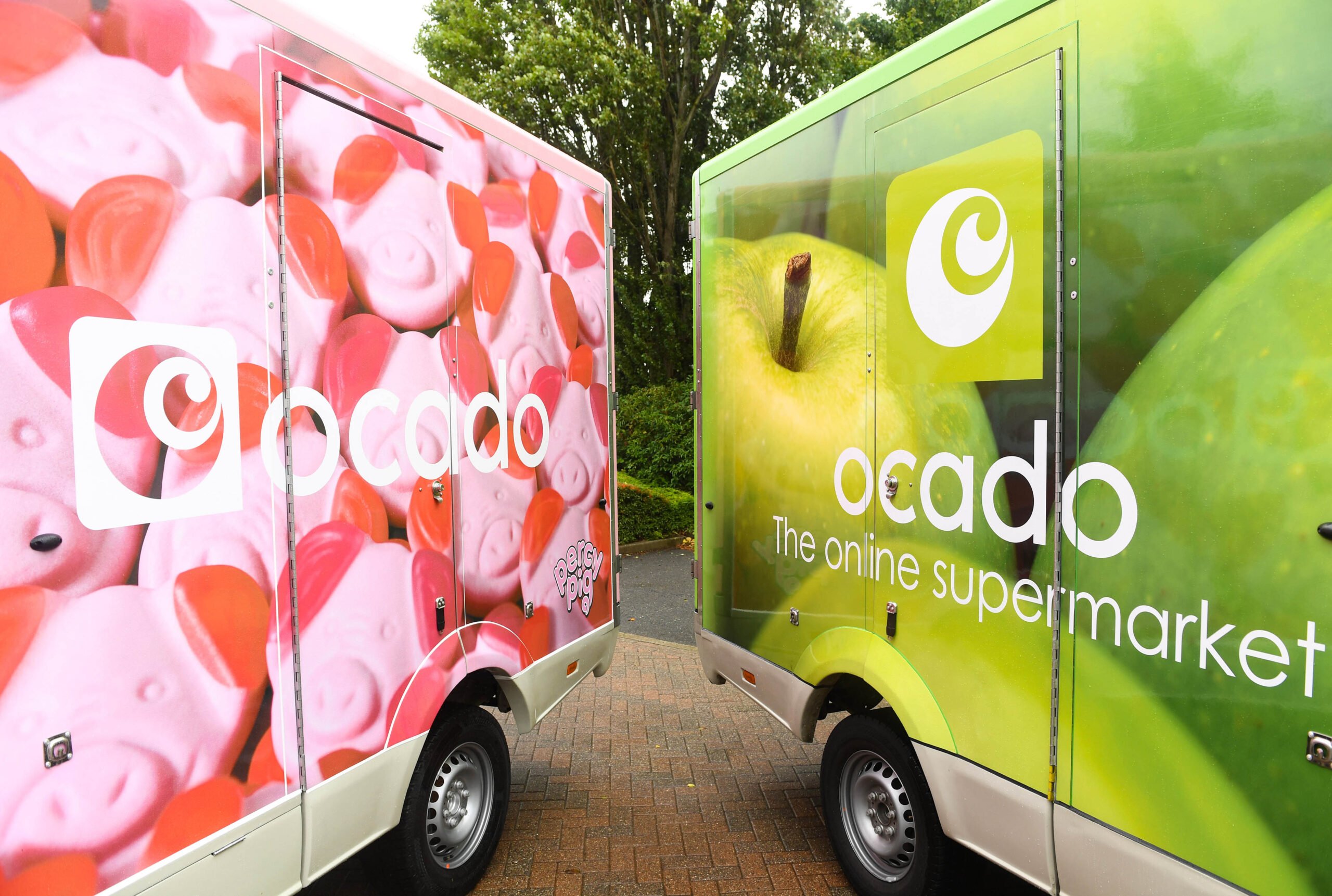 Two Ocado Group trucks with different supermarket logos decorating them.