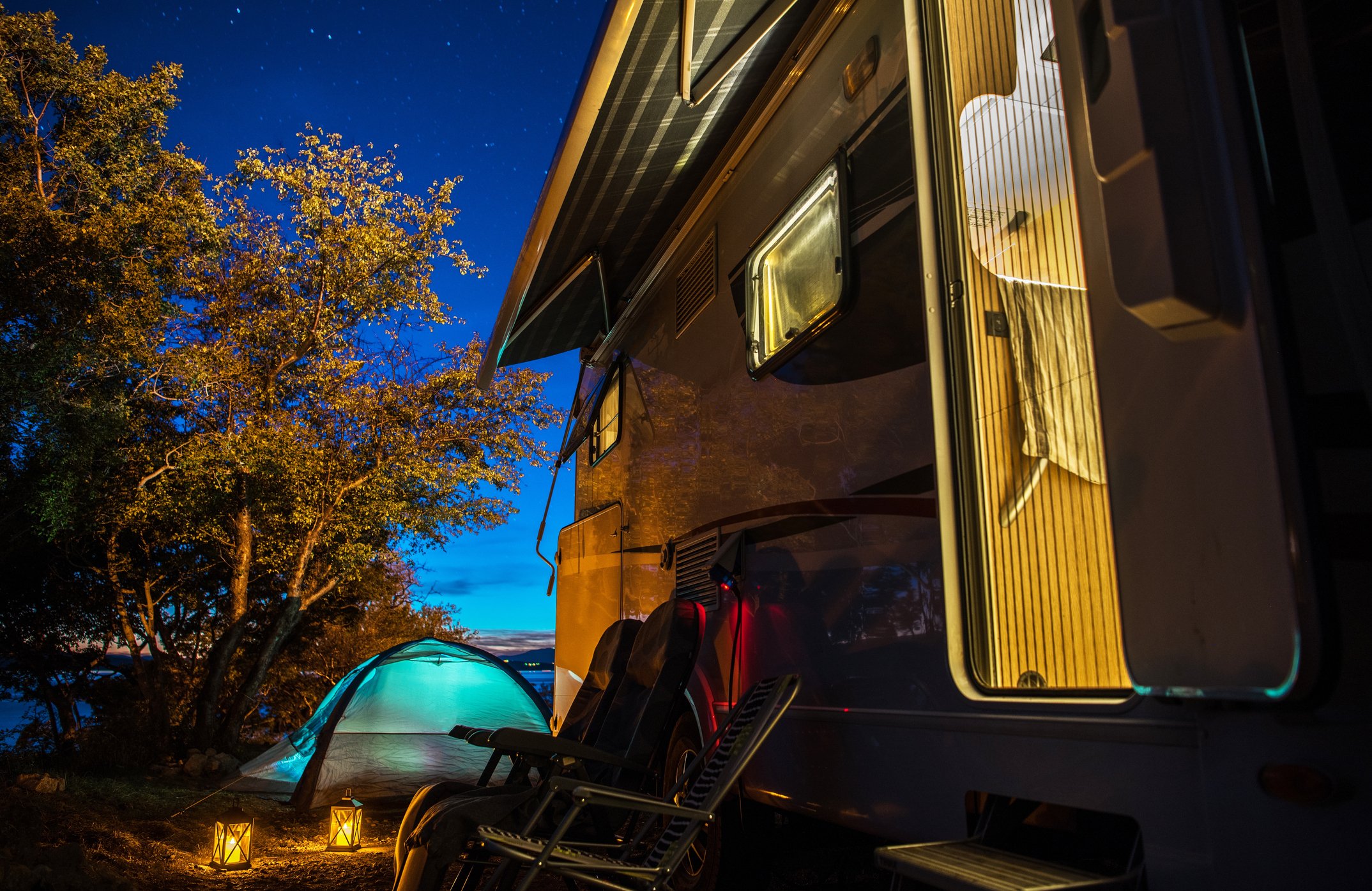 An RV and a nearby pitched tent are seen at night.