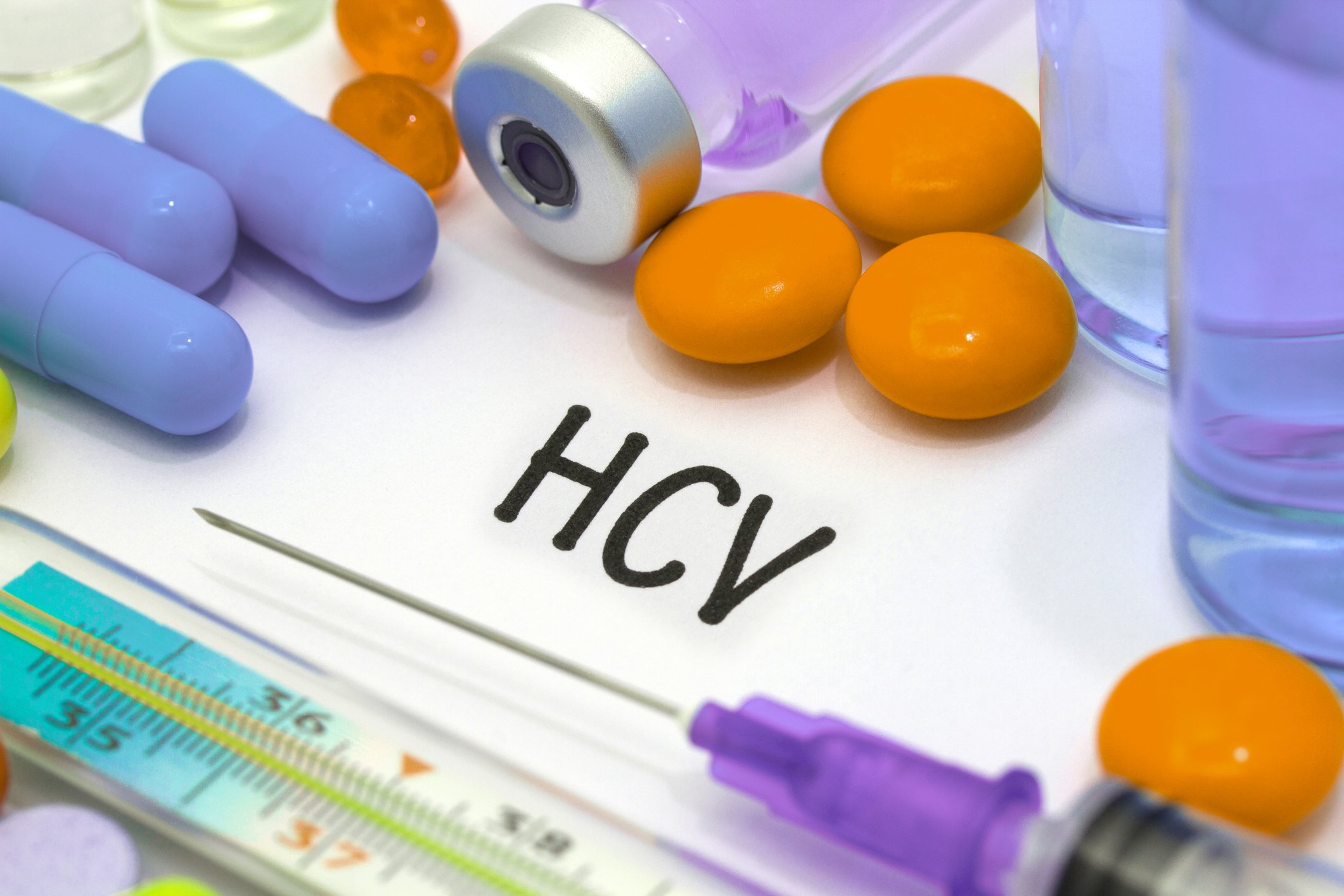 several different colored pills, a syringe, and the letters HCV on paper