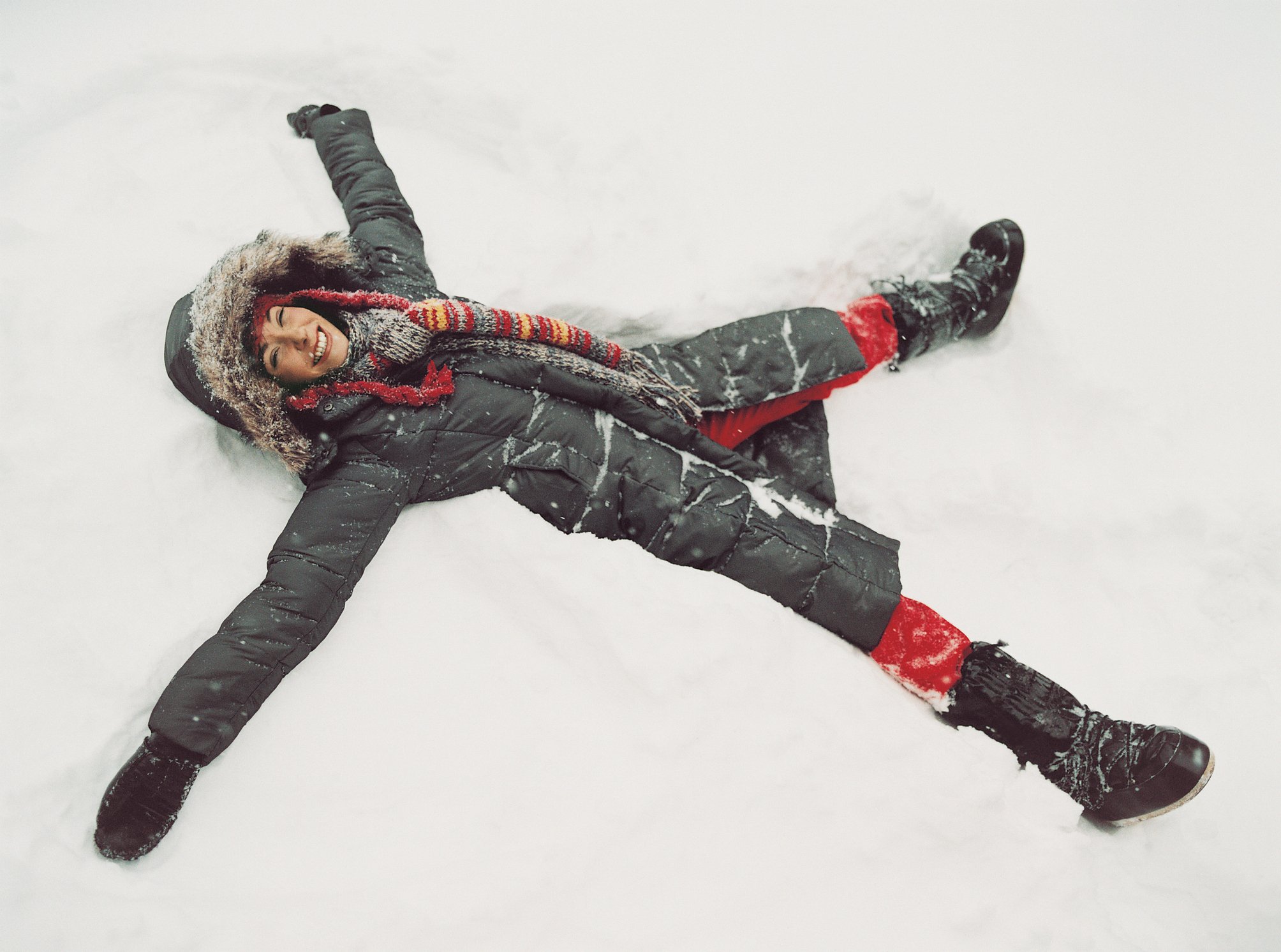A woman in a parka lies in the snow making a snow angel