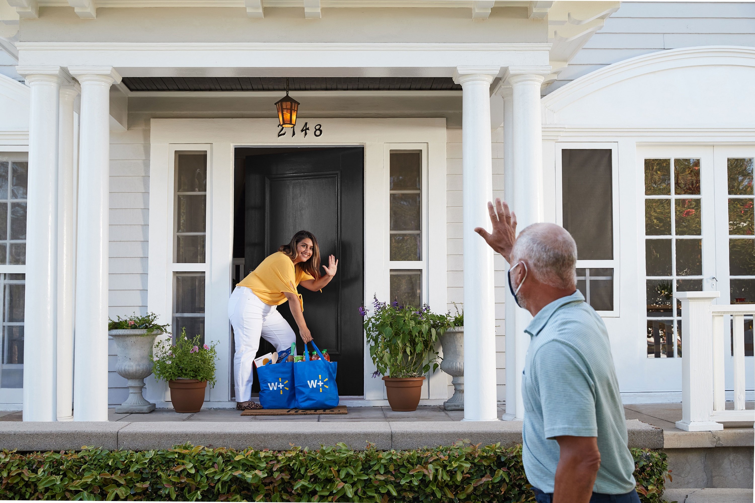 Walmart customer picking up a delivery off her front porch as the delivery person waves from a distance.