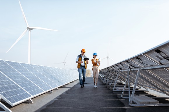 Engineers on a solar power plant with several windmills in the background.