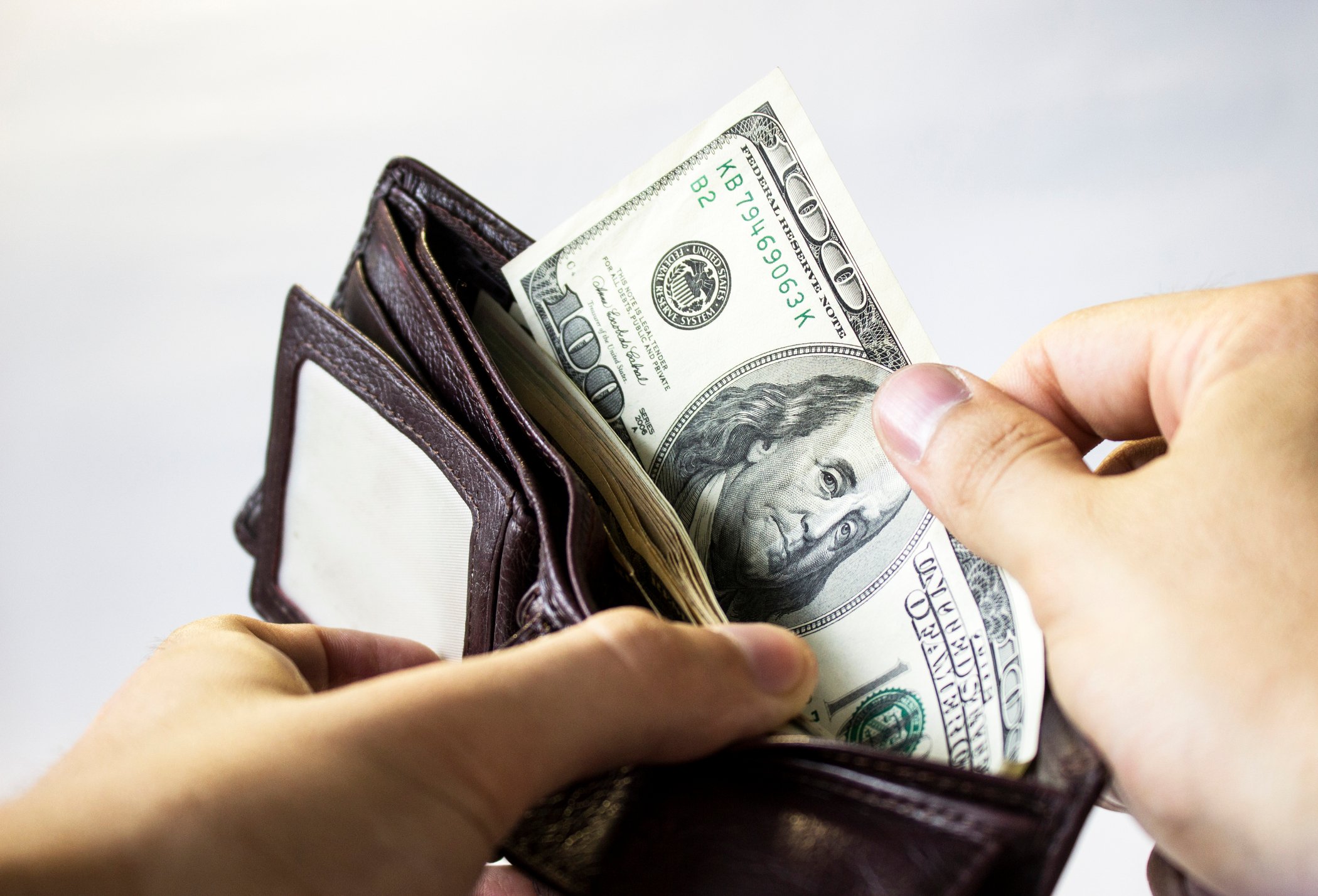 A person pulling a $100 bill out of a wallet.