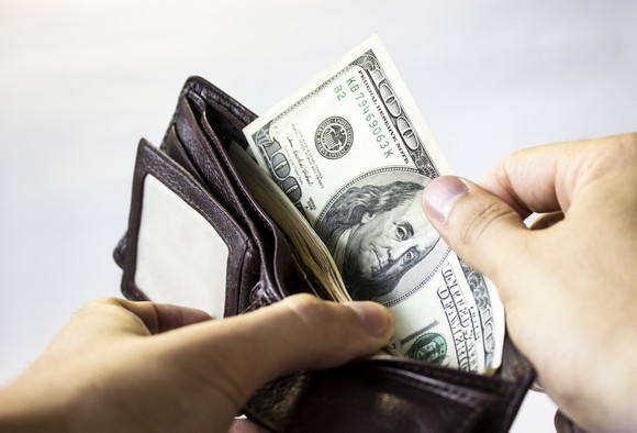 A person pulling a $100 bill out of a wallet.