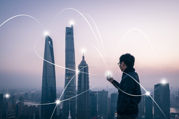 A person holding a cellphone in front of an urban skyline. 